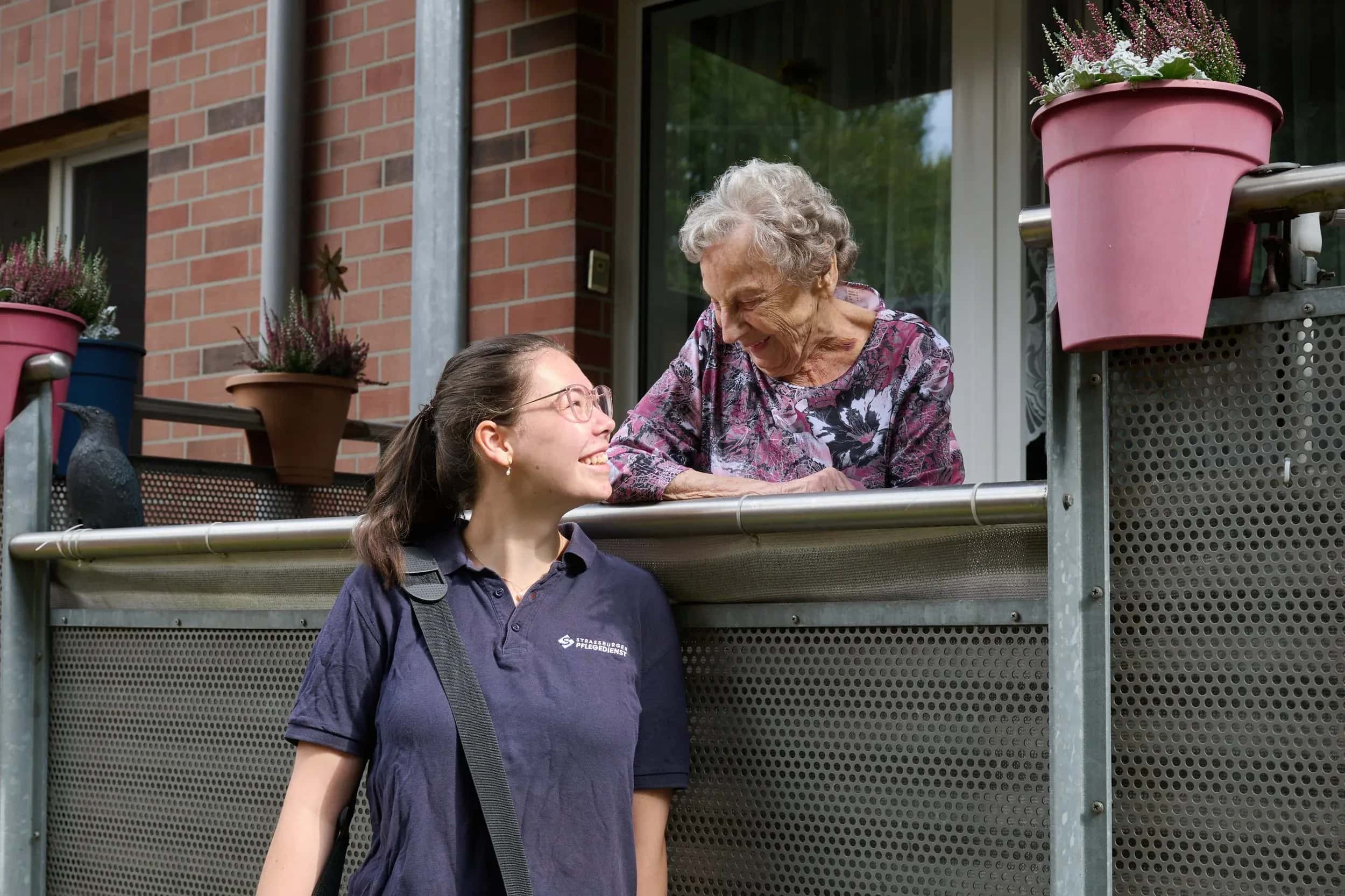 Pflegerin des Strassburger Pflegedienstes im Gespräch mit einer Seniorin am Balkon